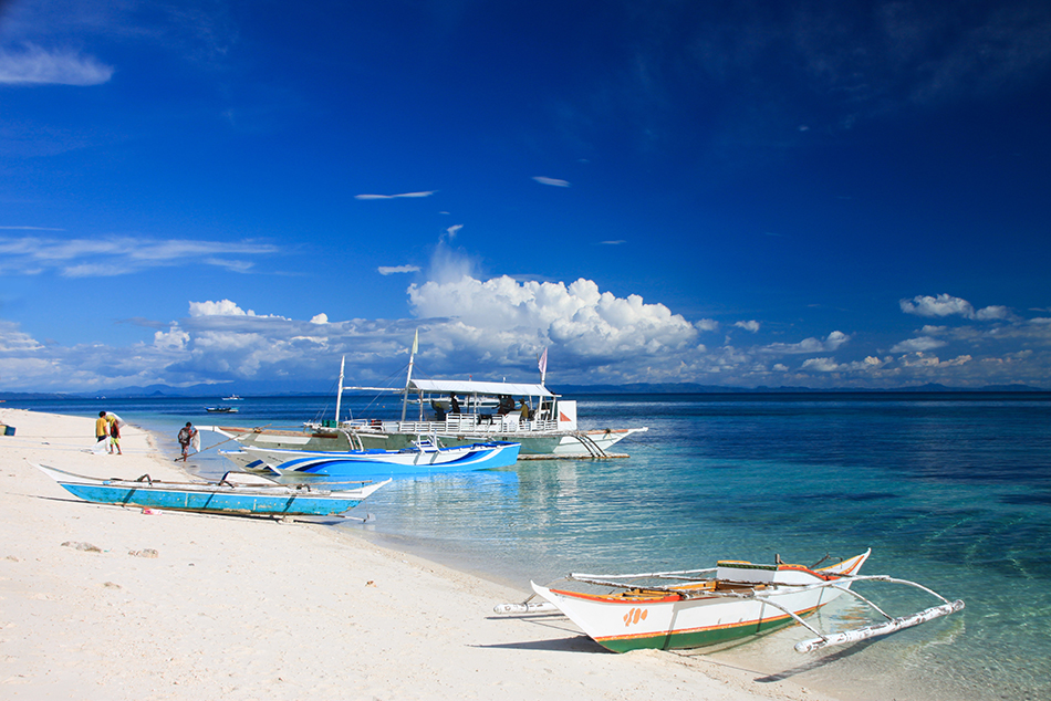 wooden boats on the sandy beach at crystal clear blue waters wit